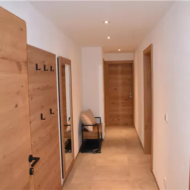 A bright hallway with wooden rollers and modern walls. On the left side, there is a chair and several doors.