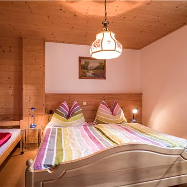 Ein gemütliches Schlafzimmer mit Holzverkleidung und zwei Betten. Die bunten Bettdecken und das typische Licht sorgen für eine einladende Atmosphäre.