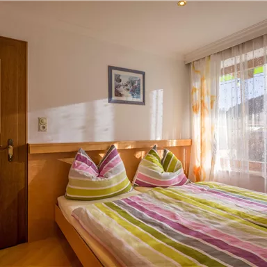 Ein gemütliches Schlafzimmer mit einem Doppelbett und bunten Kissen. Die Fenster sind hell und lassen viel Licht herein.