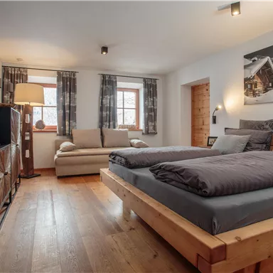 Ein modernes Schlafzimmer mit einem Doppelbett und einem gemütlichen Sofa. Die Fenster sind mit Vorhängen geschmückt und bieten viel Tageslicht.