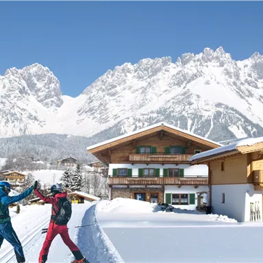 A雪-covered mountain village with large mountains in the background. Two skiers are happily celebrating in the snow.