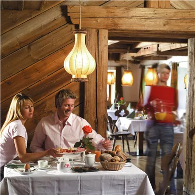 A cozy restaurant with rustic wooden interior. A couple enjoys breakfast while a waiter serves drinks.