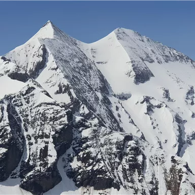 Ein majestätisches Bergpanorama mit schneebedeckten Gipfeln. Der klare blaue Himmel lässt die beeindruckende Landschaft strahlen.