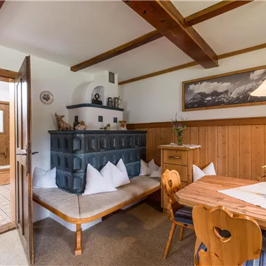 A cozy dining area with a wooden table and a rustic seating corner. There is a beautiful oven against the wall and decorative elements.