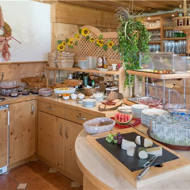 A cozy breakfast table with various wooden and stone plates, plenty of delights such as cheese, cold cuts, and fresh fruit. The warm wood accents and the decoration create an inviting atmosphere.