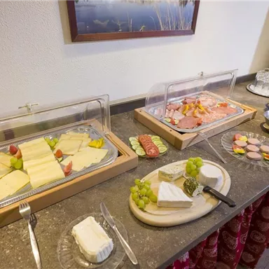 A buffet with a selection of cheese, sausage, and fresh fruit. Next to it are drinks like juice and glasses ready.