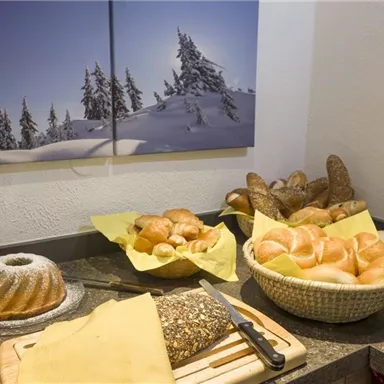 A buffet with various rolls and bread on a table. In the background, a picture of snow-covered trees hangs.