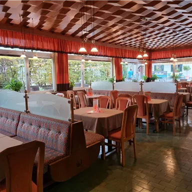 Ein gemütliches Restaurant mit Holzvertäfelung und großen Fenstern. Tische sind ordentlich gedeckt und es gibt Pflanzen im Raum.