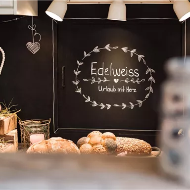 An inviting kitchen with a table on which "Edelweiss" and "Holidays with Heart" are written. Alongside fresh bread and drinks, the atmosphere is warm and cozy.
