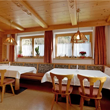 A cozy dining room with wood decor and warm colors. There are tables with white tablecloths and windows that let in a lot of light.