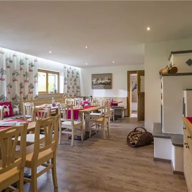 A cozy dining room with wooden chairs and tables. Bright walls and large windows create an inviting atmosphere.