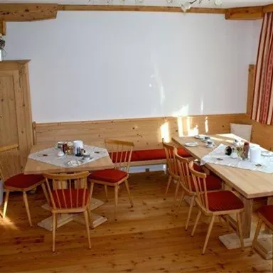 A cozy dining room with wooden tables and chairs. The walls are light, and there are plants in the room.