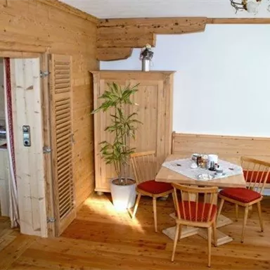 A cozy living room with wood paneling and modern furniture. Chairs are ready at the table, while a plant in the room adds a touch of green.