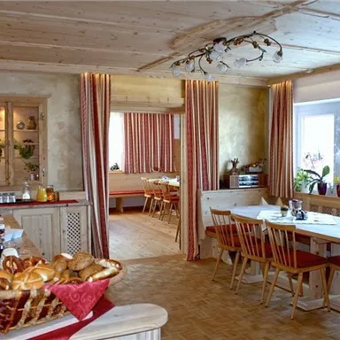 A cozy dining area with wood decor and large windows. The table is set with bread rolls and fresh ingredients.