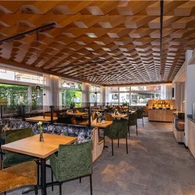 A modern restaurant with bright wooden paneling and comfortable seating. Large windows let in plenty of light and offer a view of the outdoor areas.