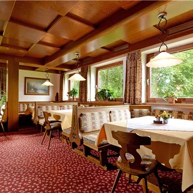 Ein gemütliches Restaurant mit Holzmöbeln und gepolsterten Sitzbänken. Die Fenster bieten einen Blick ins Grüne und es herrscht eine einladende Atmosphäre.