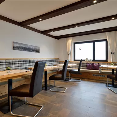 Ein modernes Restaurant mit Holztischen und stilvollen Stühlen. Große Fenster sorgen für viel Tageslicht und eine einladende Atmosphäre.