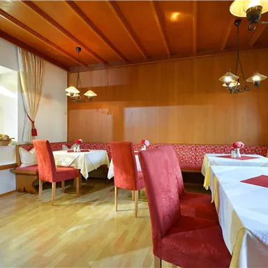 A cozy restaurant with wooden elements and red chairs. The tables are decorated and there is plenty of natural light.