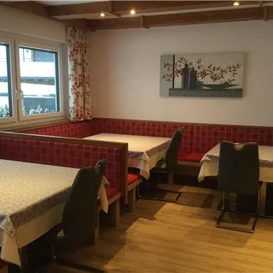 A cozy restaurant with wooden tables and red benches. Decorative pictures hang on the walls, and the windows let in plenty of light.