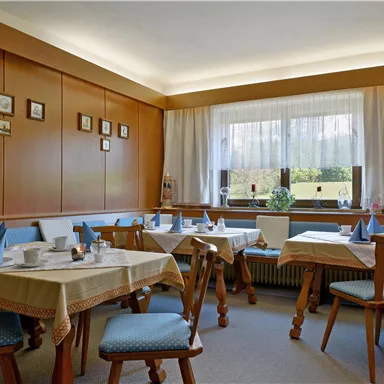 A cozy dining room with bright tables and chairs. Light falls on the decorated wall through the windows.