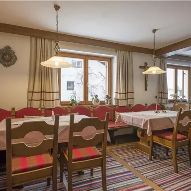 Ein gemütlicher Speisesaal mit einem großen Tisch und Holzbänken. Die Fenster sind hell und lassen viel Licht herein.