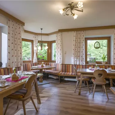 A cozy restaurant with wooden tables and brightly striped benches. The windows offer a view of the outside and allow plenty of daylight in.