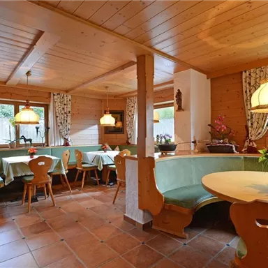 Ein gemütlicher Restaurantbereich mit Holzmöbeln und grünen Tischen. Die Fenster lassen viel Tageslicht herein und schaffen eine einladende Atmosphäre.