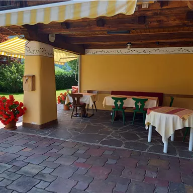 An inviting terrace with tables and chairs under a parasol. Colorful flowers and green grass create a lovely atmosphere.