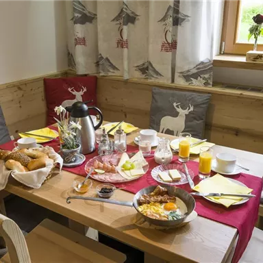 A beautifully set breakfast table in a cozy environment. There are fresh rolls, drinks, and a hearty breakfast dish.