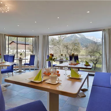 Ein modernes Café mit blauen Sitzbänken und Tischen. Durch die großen Fenster blickt man auf eine schöne Berglandschaft.
