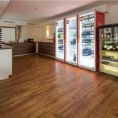 A modernly designed room with a wooden floor and a reception area. Refrigerators with drinks and snacks are along the wall.