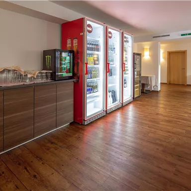 A cozy room with wooden floors and refrigerators offering snacks and drinks. The atmosphere is bright and inviting.