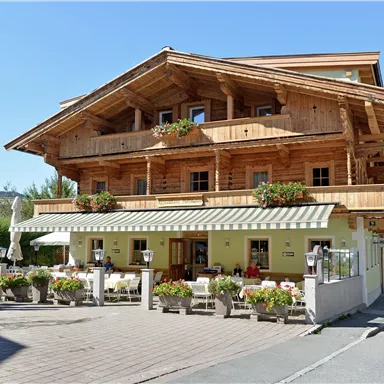 Ein charmantes Holzhaus mit drei Etagen in bayerischem Stil. Vor dem Haus sind Blumen und sonnige Terrassen zum Entspannen.