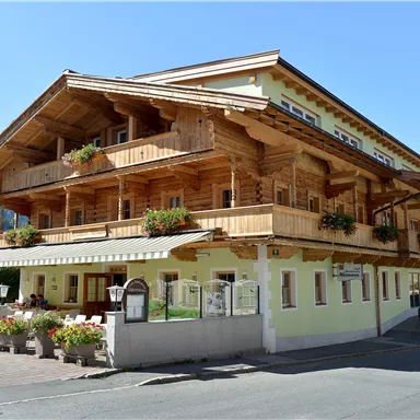 Ein charmantes Holzgebäude mit mehreren Balkonen und blühenden Blumen. Es steht in einer ruhigen Gegend mit Bergen im Hintergrund.