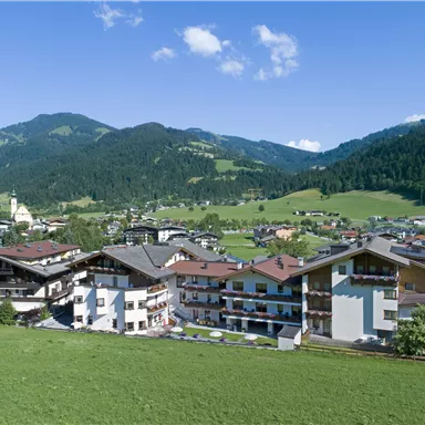 A picturesque mountain landscape with traditional buildings and green meadows. In the background, majestic mountains and a clear blue sky can be seen.