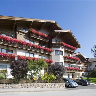 A charming building in alpine style with colorful flower balconies. The surroundings are green and inviting, perfect for a relaxing stay.