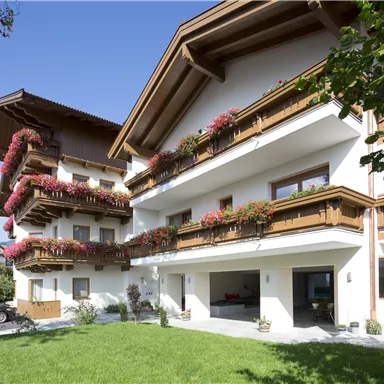 A picturesque building with balconies adorned with blooming plants. The green lawn and clear sky give the scene an inviting atmosphere.