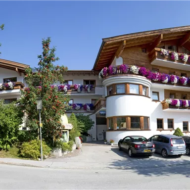 A picturesque hotel with balconies adorned with colorful flowers. Surrounded by trees and a clear blue sky.