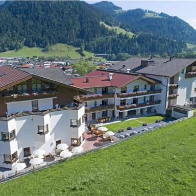 A modern hotel building surrounded by a beautiful green landscape. In the background, gentle mountains and a clear sky can be seen.