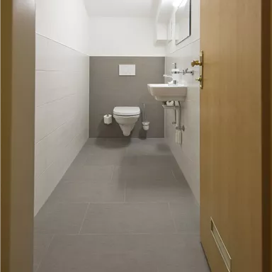 A modern bathroom with a toilet and a sink. The walls are light and the floor tiles are gray.