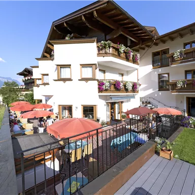 An inviting hotel with terraces and sun umbrellas. The surroundings are green and the mountains are visible in the background.