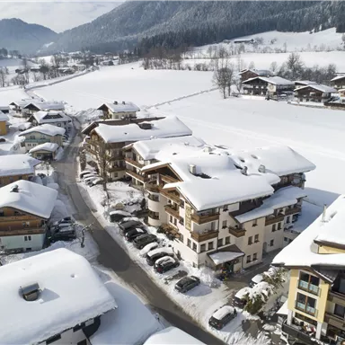 A snowy landscape with charming houses. In the background, snow-covered mountains and a clear sky can be seen.