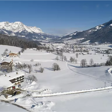 A snowy landscape with mountains in the background. Farmhouses and a quiet path run through the winter scenery.