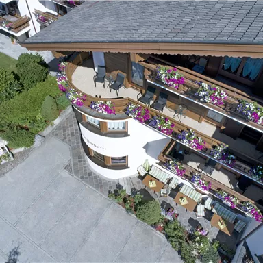 A charming hotel with beautiful balconies adorned with colorful flowers. In the foreground, cozy seating is visible on the terrace.