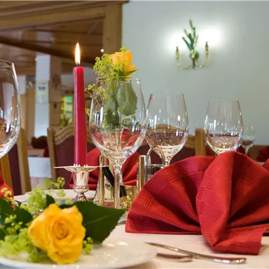 An elegantly set table with red napkins and wine glasses. A rose and a candle create a romantic atmosphere.
