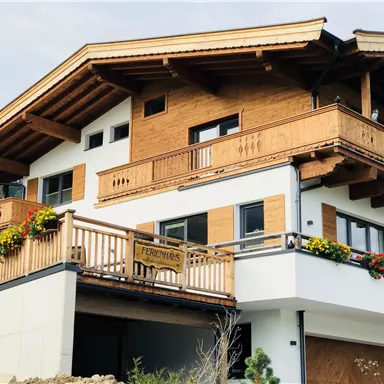 Ein modernes Chalet mit Holzverkleidung und mehreren Balkonen. Bunte Blumen schmücken die Fassade und sorgen für eine einladende Atmosphäre.