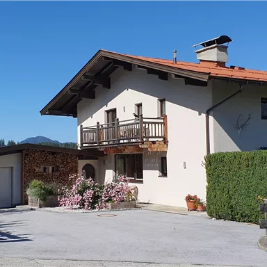 A charming house with a red gable roof and a beautifully designed outdoor area. Surrounded by green trees and flowers, it offers an inviting atmosphere.