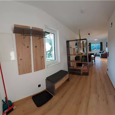 A bright hallway with wooden floor and modern furniture. On the wall, there is a coat rack and a shelf.