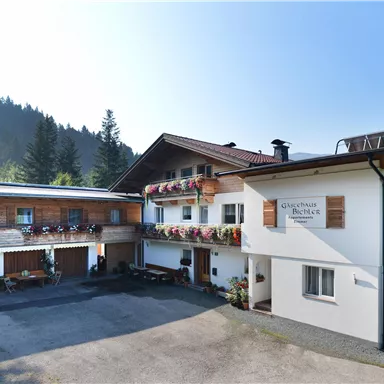 A cozy guesthouse in a mountainous setting. The building has balconies with flowers and a bright facade.