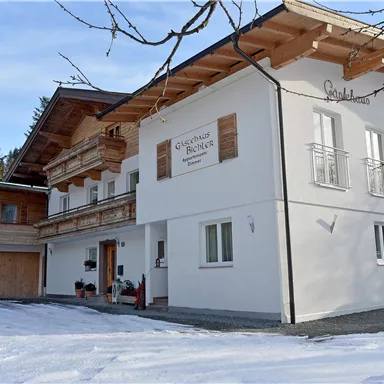 A modern house in alpine style, surrounded by snow and trees. The facade is bright and inviting, with wooden details.